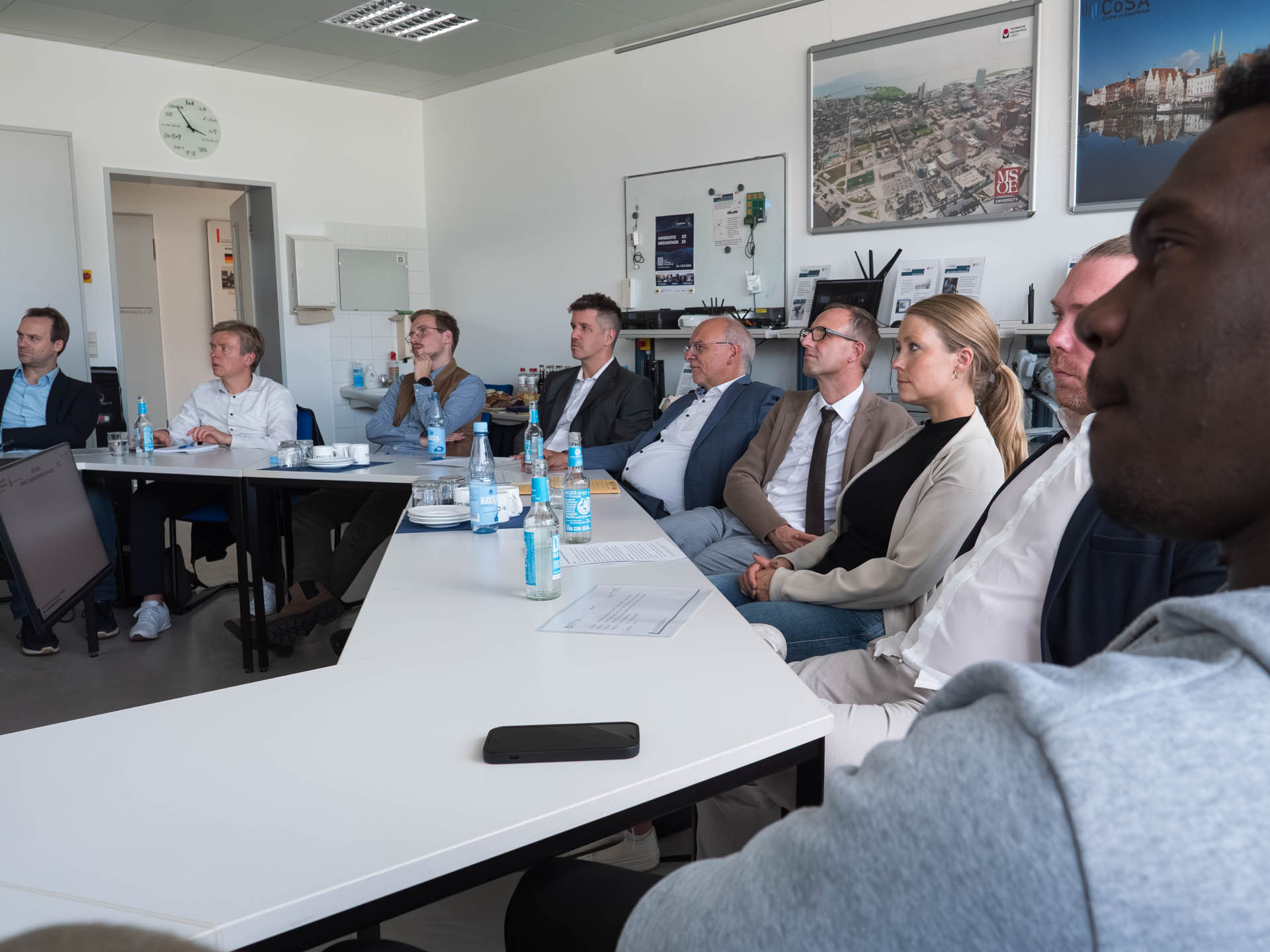 Neun Personen sitzen an einem großen Tisch und schauen in die gleiche Richtung